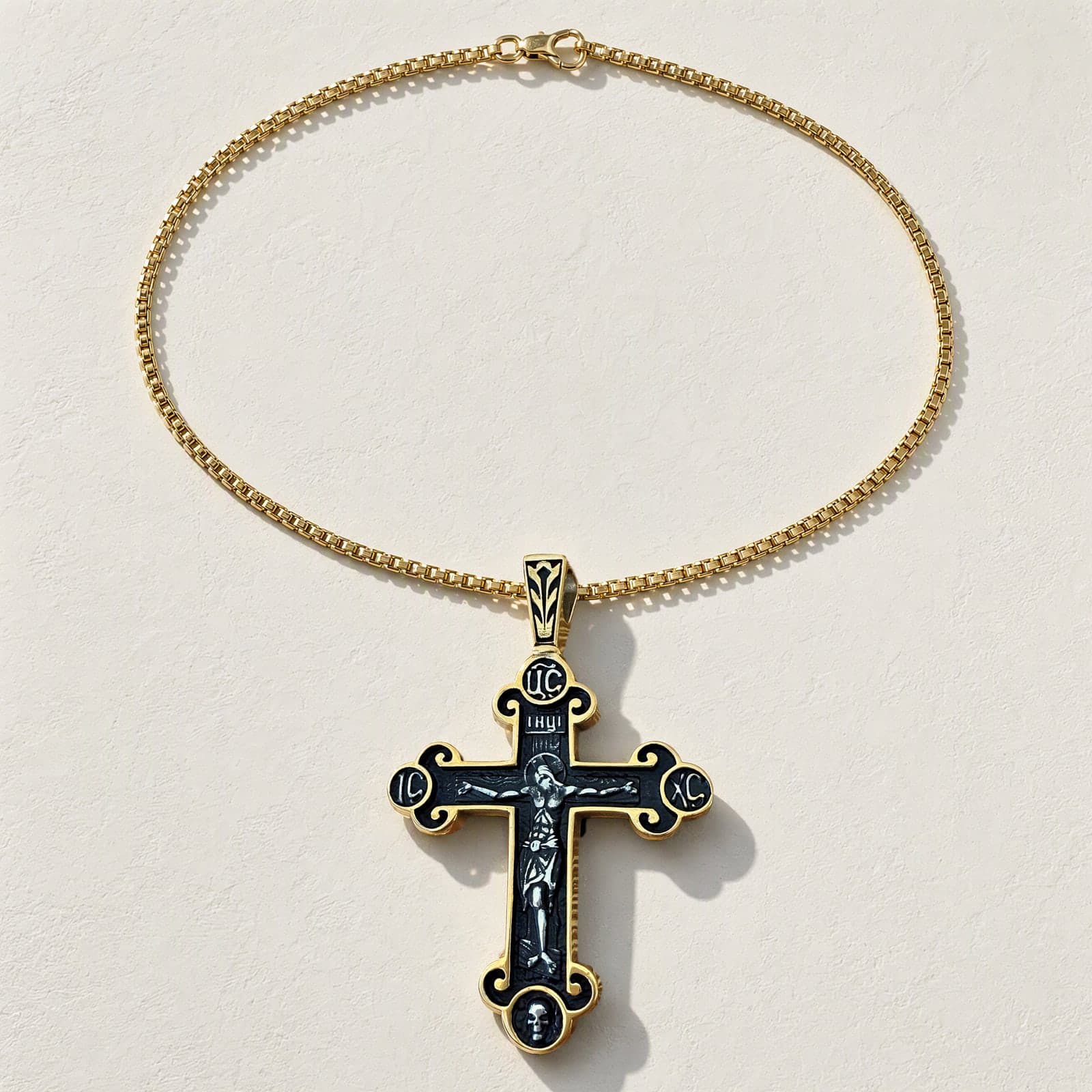 Orthodox Crucifix (Roundels) - Black&Gold Color - Stainless Steel Cross laid flat with its plain gold-tone box chain on a white plaster surface.