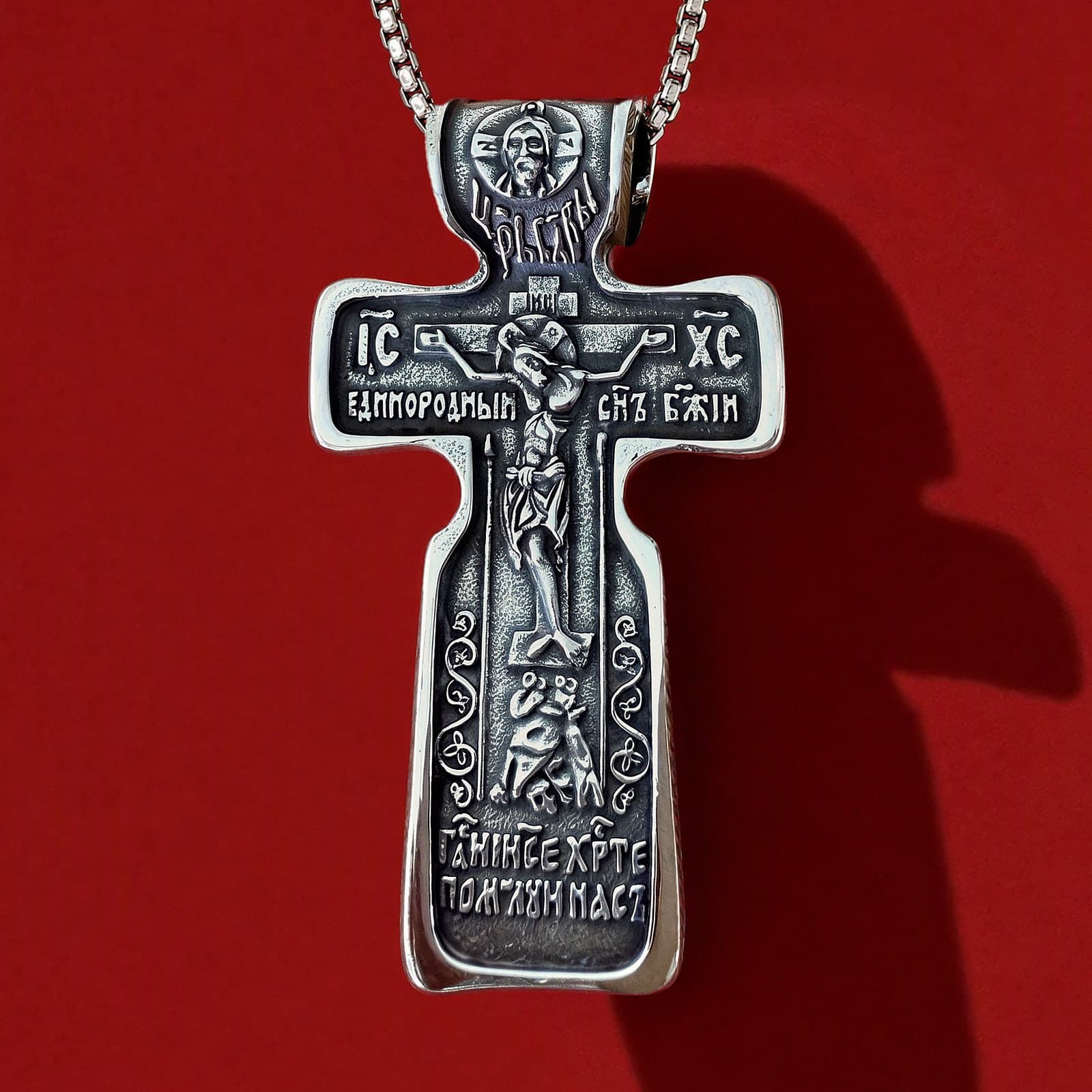 Orthodox Crucifix (Jesus Prayer, Dark) - Silver Color - 60cm Chain - Stainless Steel Cross: a silver-tone stainless steel Orthodox crucifix with a rounded foot and relief of the Crucifixion on a silver-tone box chain, against an oxblood backdrop.