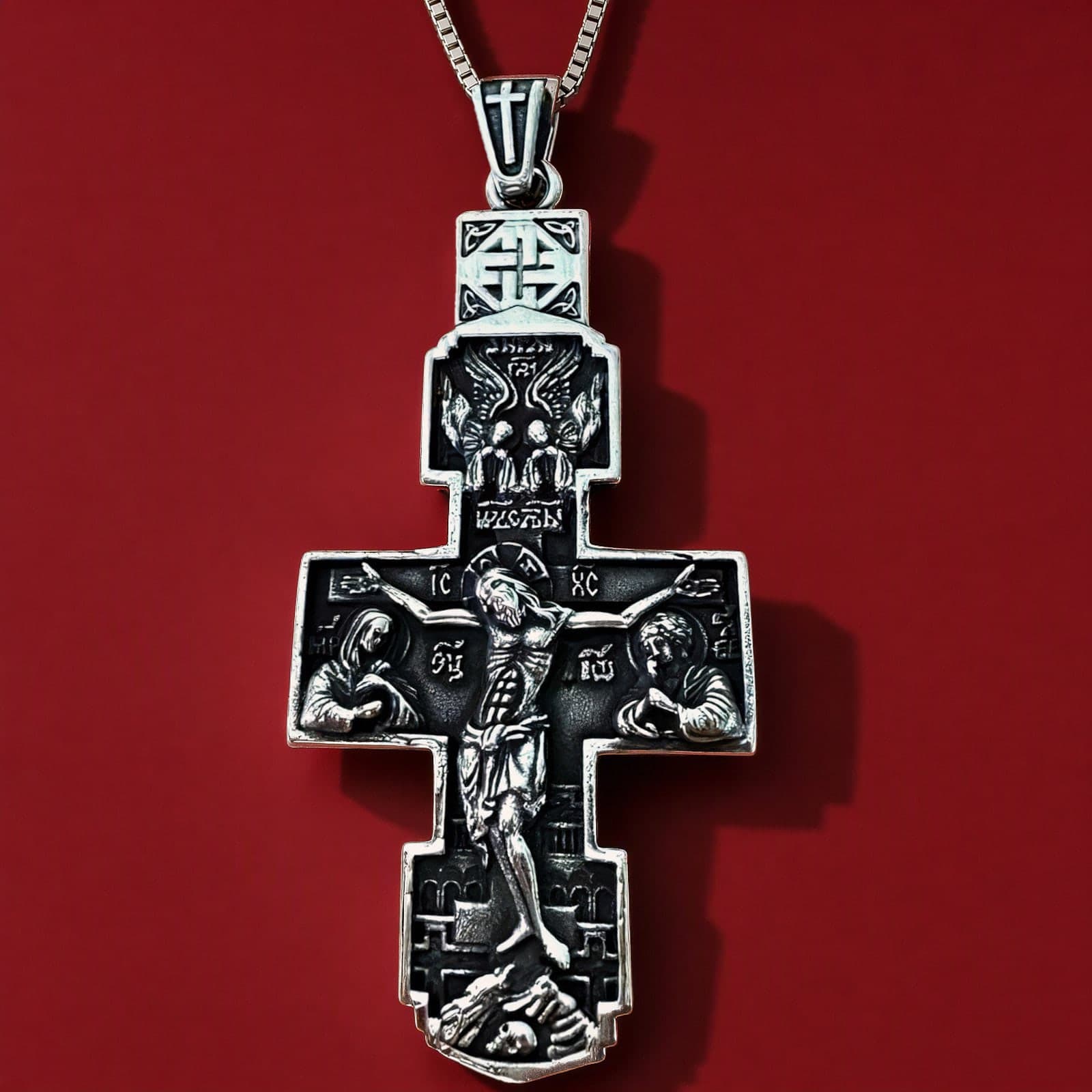 Orthodox Crucifix - Silver Color - Stainless Steel Cross 20.2g: a large silver-tone stainless steel Orthodox crucifix with a tall bail topped by a small cross, deep relief of the Crucifixion with angels on a plain silver-tone box chain (shown on a chain), against an oxblood backdrop.