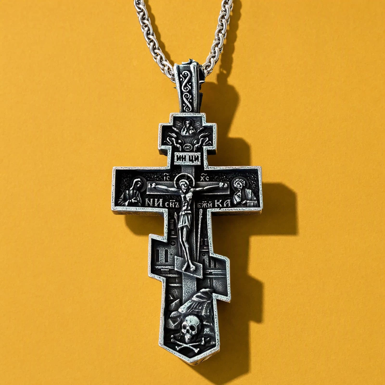 Orthodox Crucifix (Mary and St John, Dark) - Silver Color - 60cm Chain - Stainless Steel Cross: a blackened silver-tone stepped Orthodox crucifix with deep relief on a silver-tone wheat chain, against an ochre backdrop.