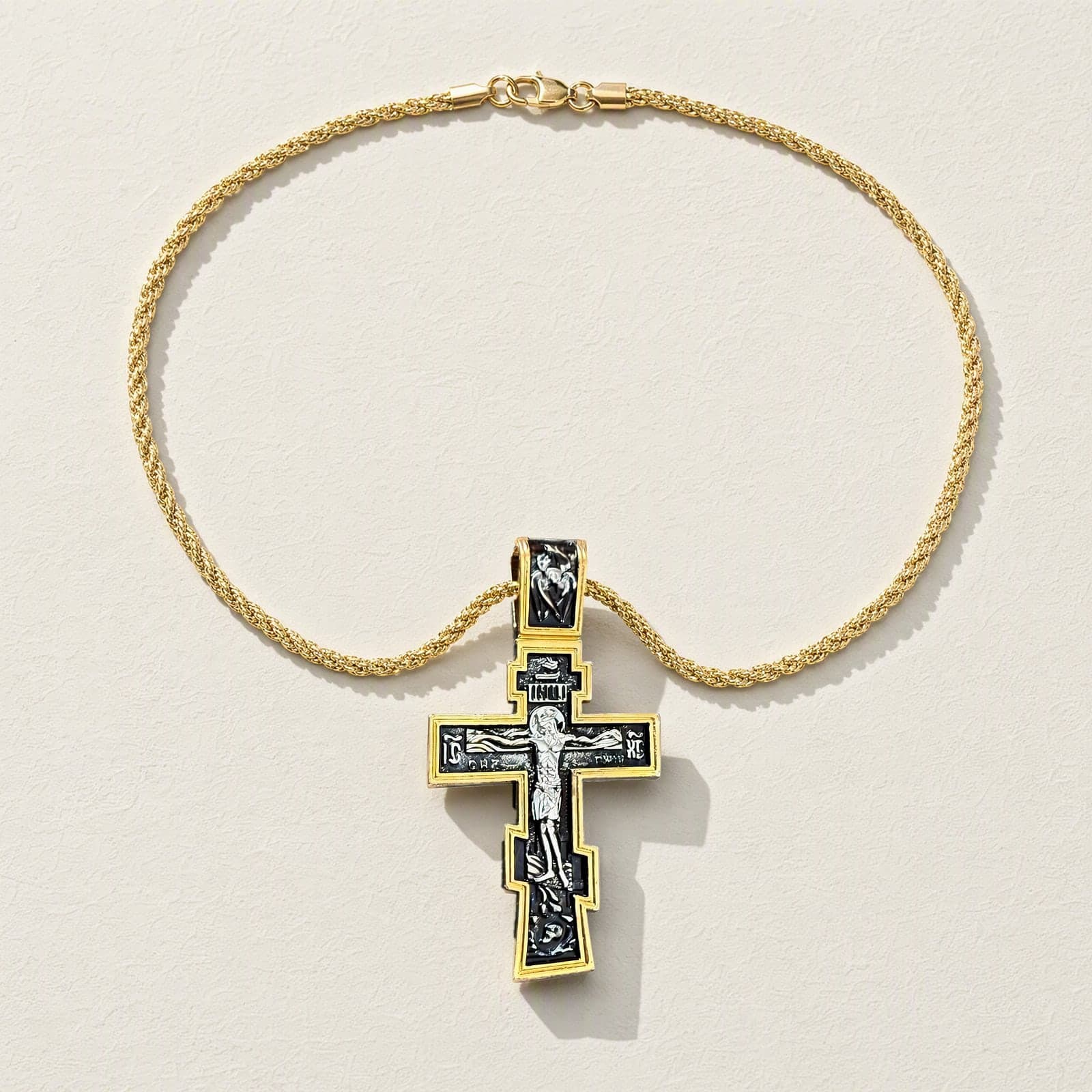 Orthodox Crucifix - Black&Gold Color - 60cm Chain - Stainless Cross laid flat with its gold-tone rope chain on a white plaster surface.