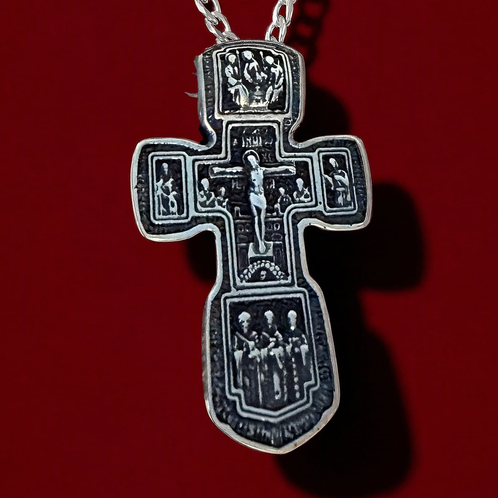 Orthodox Crucifix (Holy Trinity) - Silver Color - Stainless Steel Cross: an antiqued silver-tone Orthodox crucifix with a rounded foot and relief panels on a silver-tone curb chain, against an oxblood backdrop.