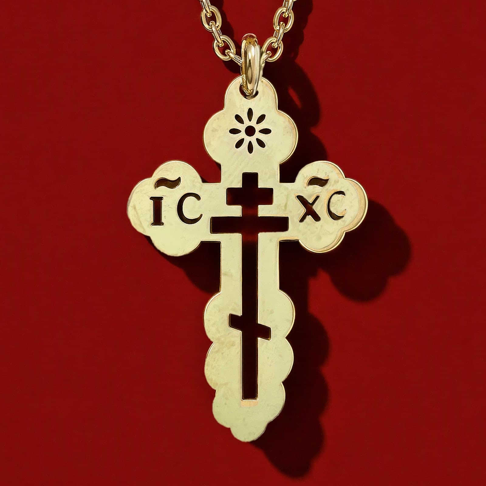 Orthodox IC XC - Gold Color - Stainless Steel Cross: a small gold-tone pierced Orthodox cross with trefoil ends, the IC XC letters and a cut-out three-bar cross on a fine gold-tone cable chain, against an oxblood backdrop.