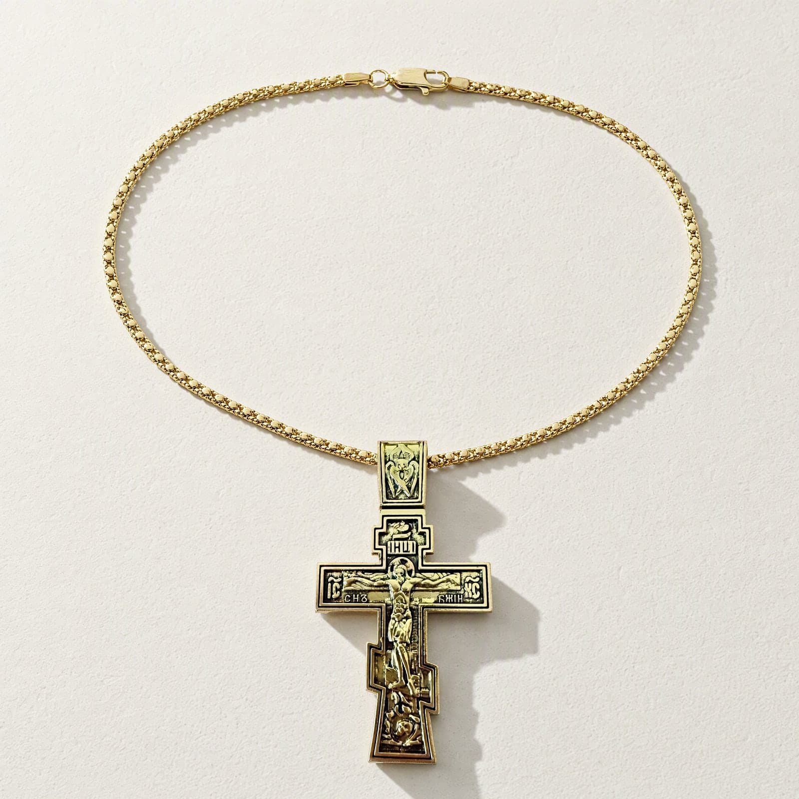 Orthodox Crucifix - 60cm Chain - Gold Color - Stainless Steel Cross laid flat with its gold-tone chain on a white plaster surface.