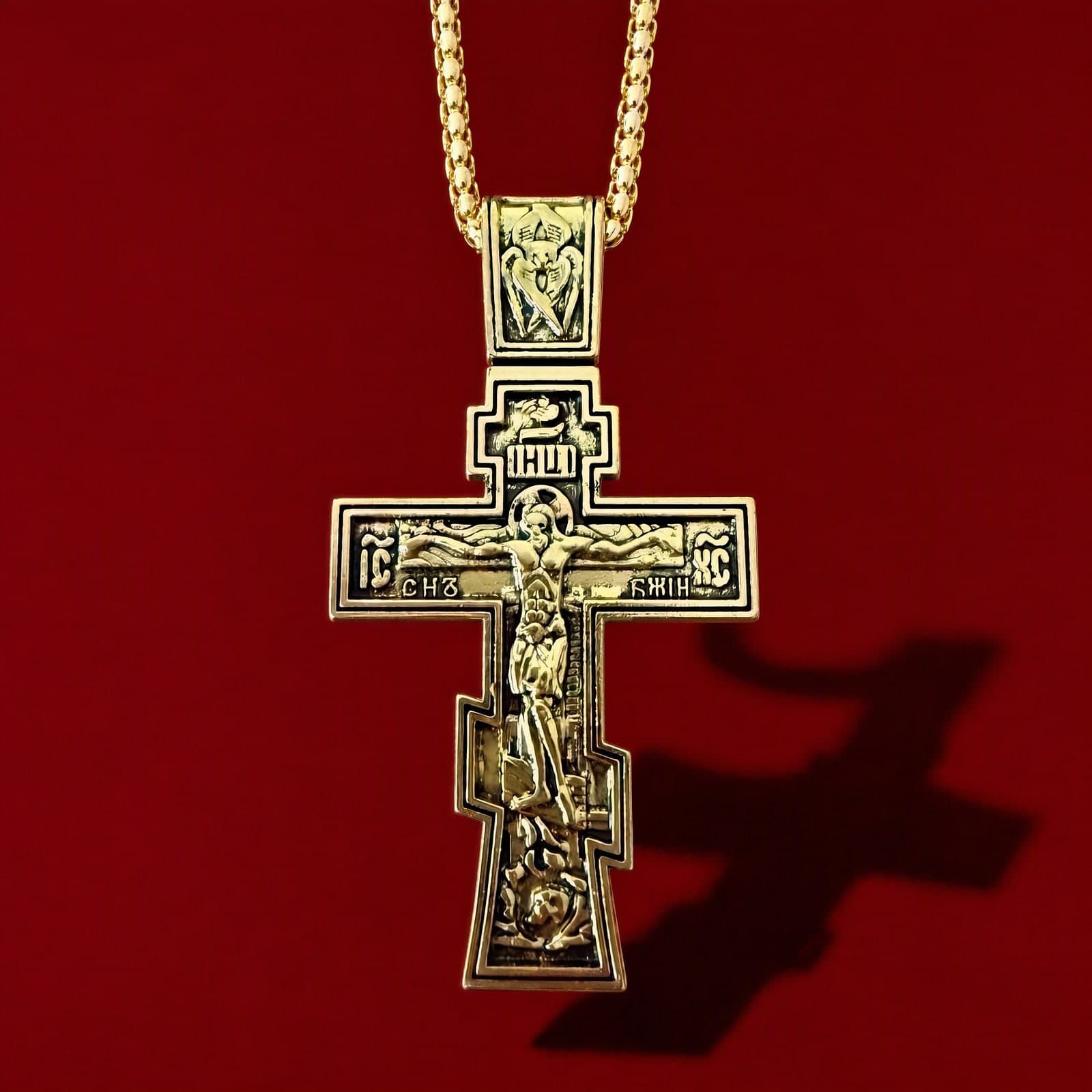 Orthodox Crucifix - 60cm Chain - Gold Color - Stainless Steel Cross: a gold-tone stepped Orthodox crucifix with fine relief of the Crucifixion on a gold-tone chain, against an oxblood backdrop.