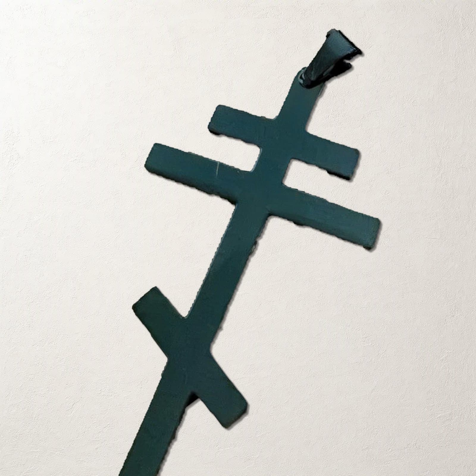 Close-up of the Orthodox Crucifix - Black Color - 60cm Chain - Stainless Steel Cross on a white plaster surface.