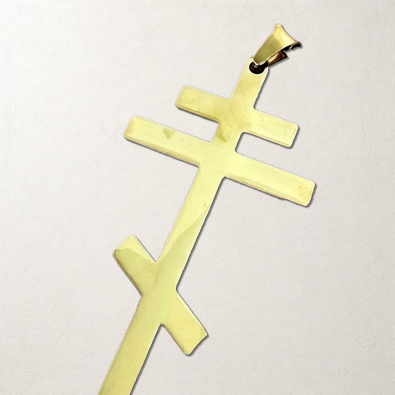 Close-up of the Orthodox Crucifix - Gold Color - 60cm Chain - Stainless Steel Cross on a white plaster surface.