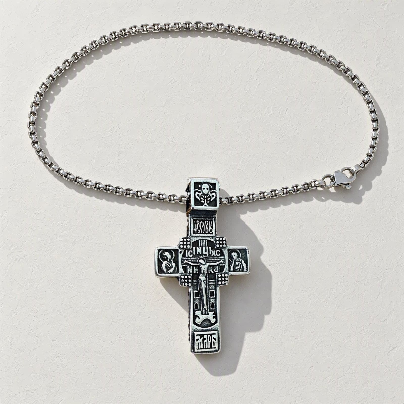 Orthodox Crucifix (Studded) - Silver Color - 60cm Chain - Stainless Steel Cross laid flat with its silver-tone box chain on a white plaster surface.