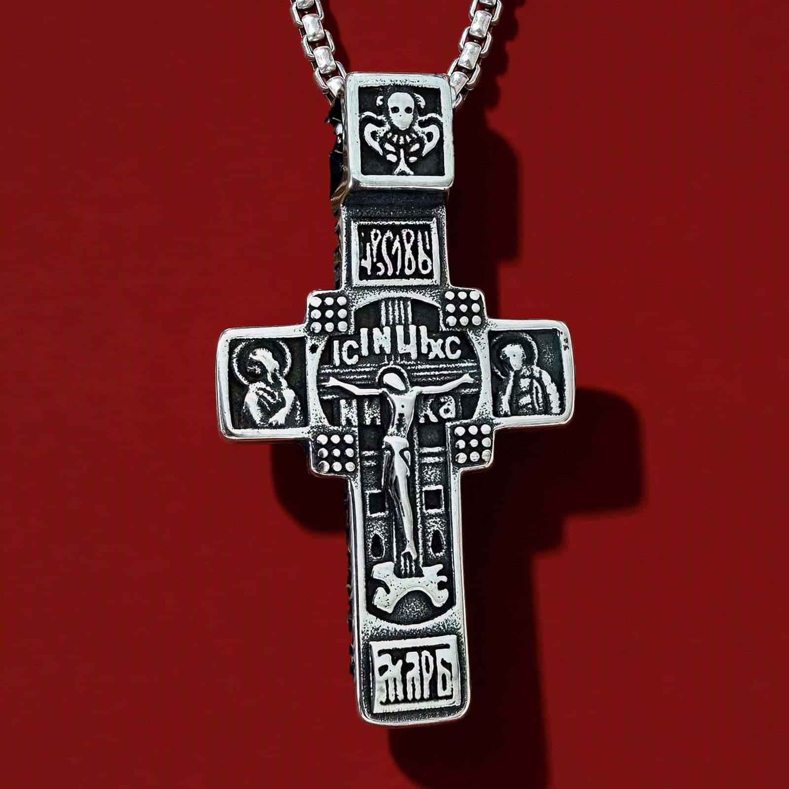Orthodox Crucifix (Studded) - Silver Color - 60cm Chain - Stainless Steel Cross: an antiqued silver-tone Orthodox crucifix with relief of saints on the arms on a silver-tone box chain, against an oxblood backdrop.