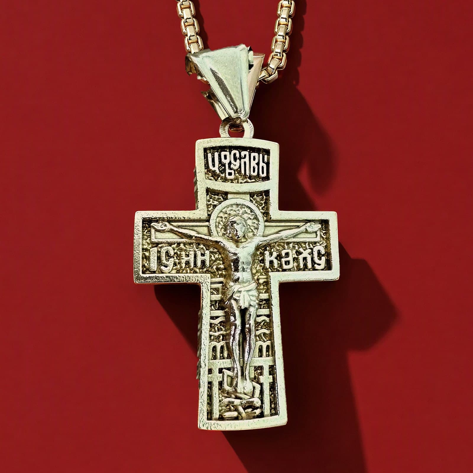 Orthodox Crucifix (King of Glory) - Gold Color - Stainless Steel Cross: a gold-tone Orthodox crucifix with relief of the Crucifixion and a tall bail on a gold-tone box chain, against an oxblood backdrop.