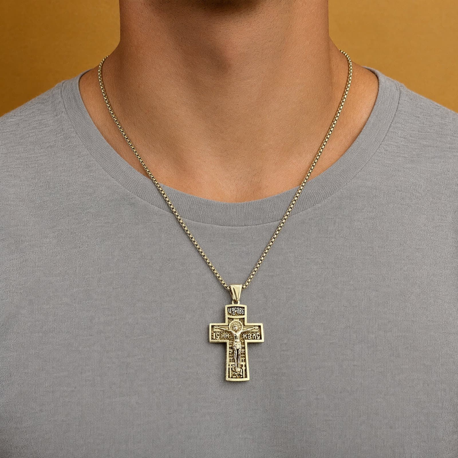 Orthodox Crucifix (King of Glory), gold-tone stainless steel cross worn at its true size (5.5 cm) on a gold-tone box chain, close crop of the chest.