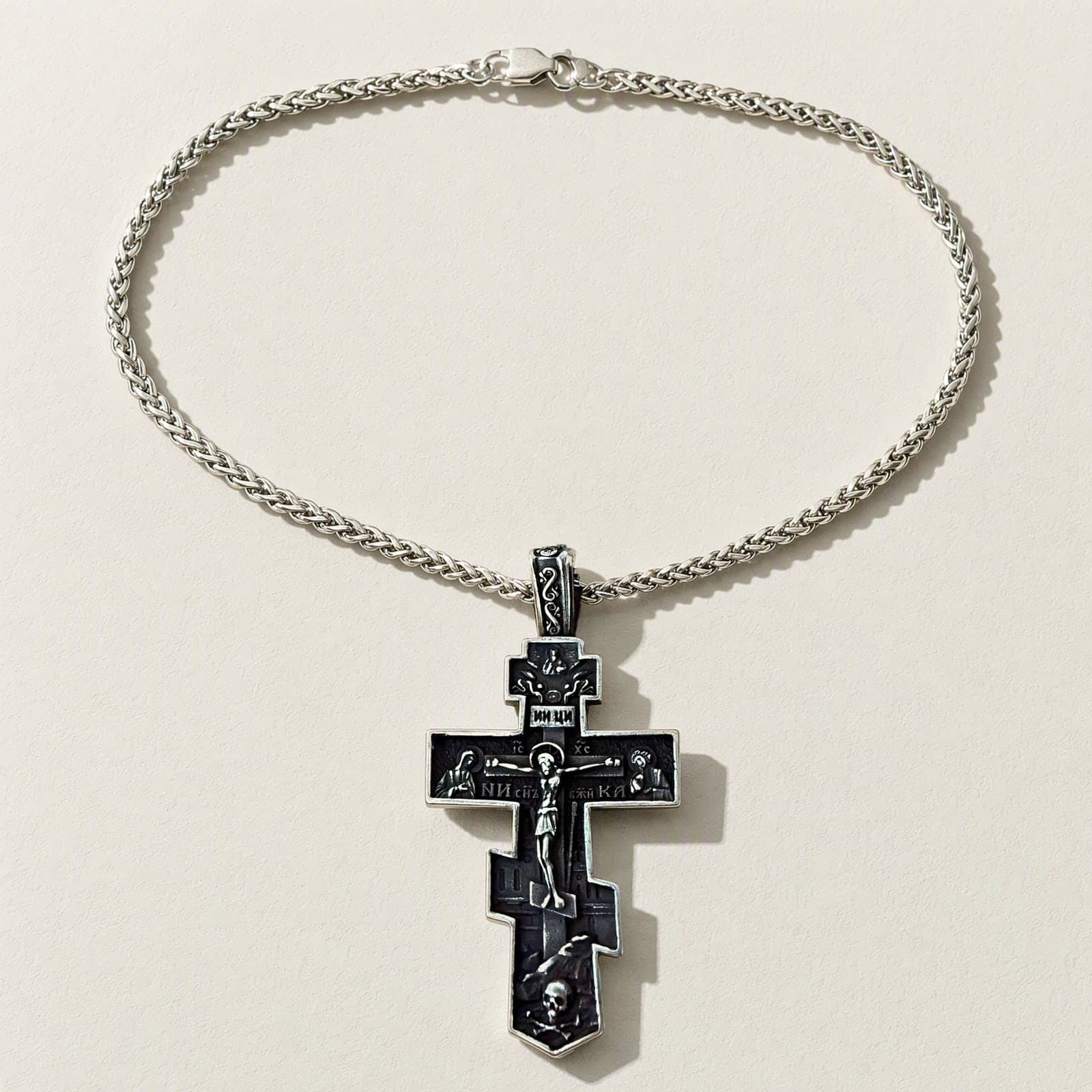 Orthodox Crucifix - Black&Silver Color - 60cm Chain - Stainless Steel Cross laid flat with its silver-tone wheat chain on a white plaster surface.