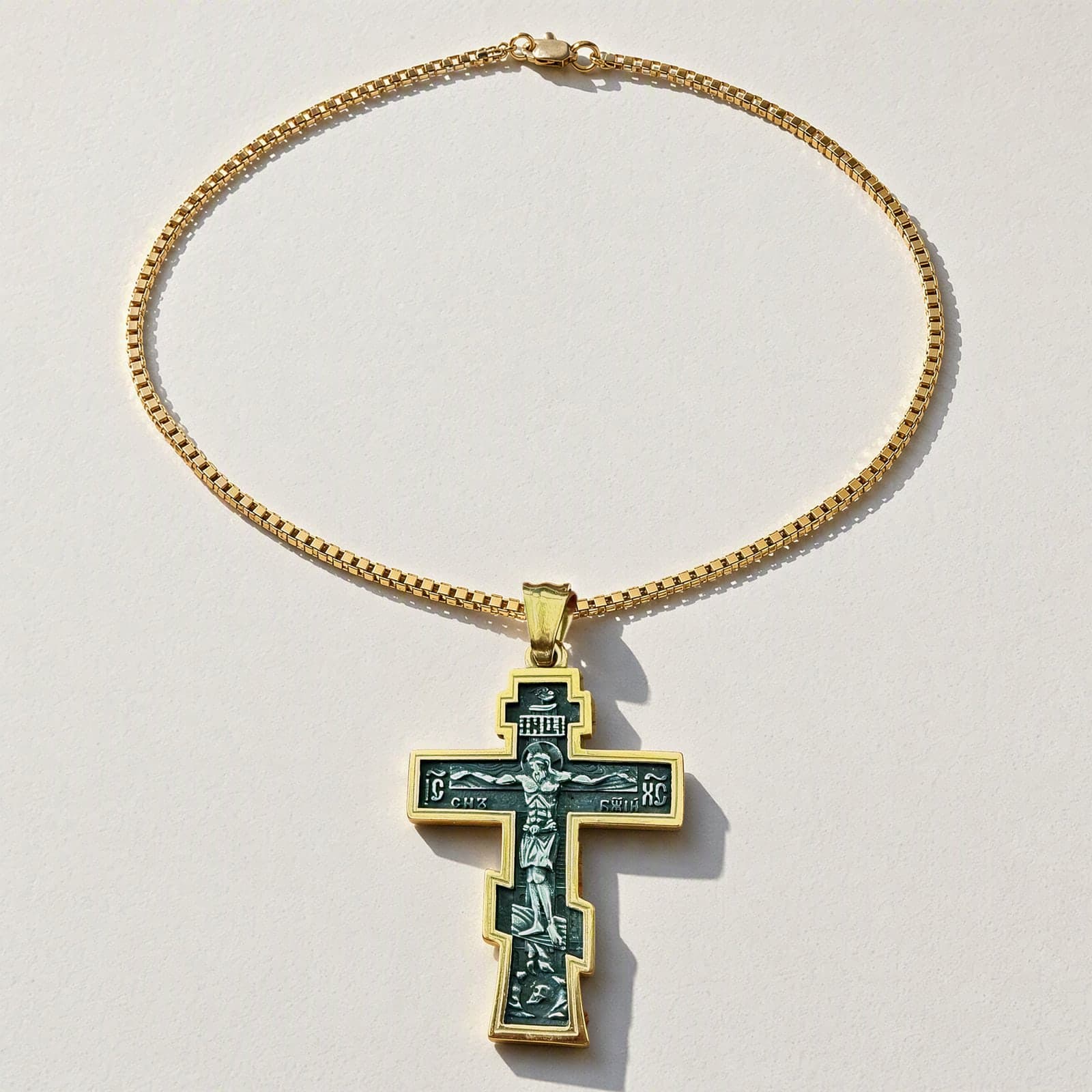 Orthodox Crucifix (Son of God) - Black&Gold Color - Stainless Steel Cross 70x39mm 20.2g laid flat with its plain gold-tone box chain on a white plaster surface.