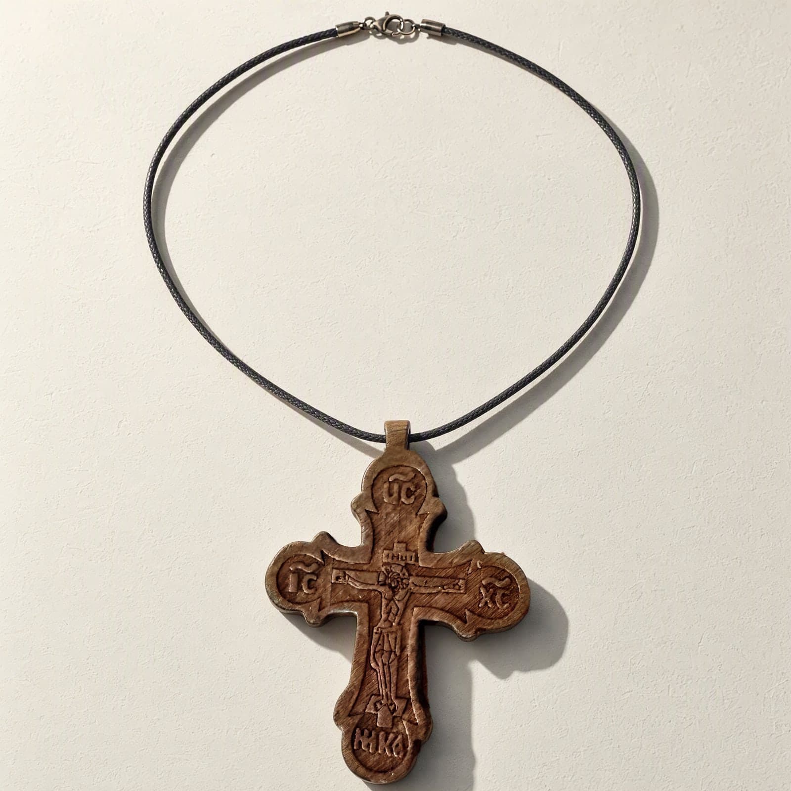 Orthodox Crucifix - Wooden Cross laid flat with its thin dark cord on a white plaster surface.