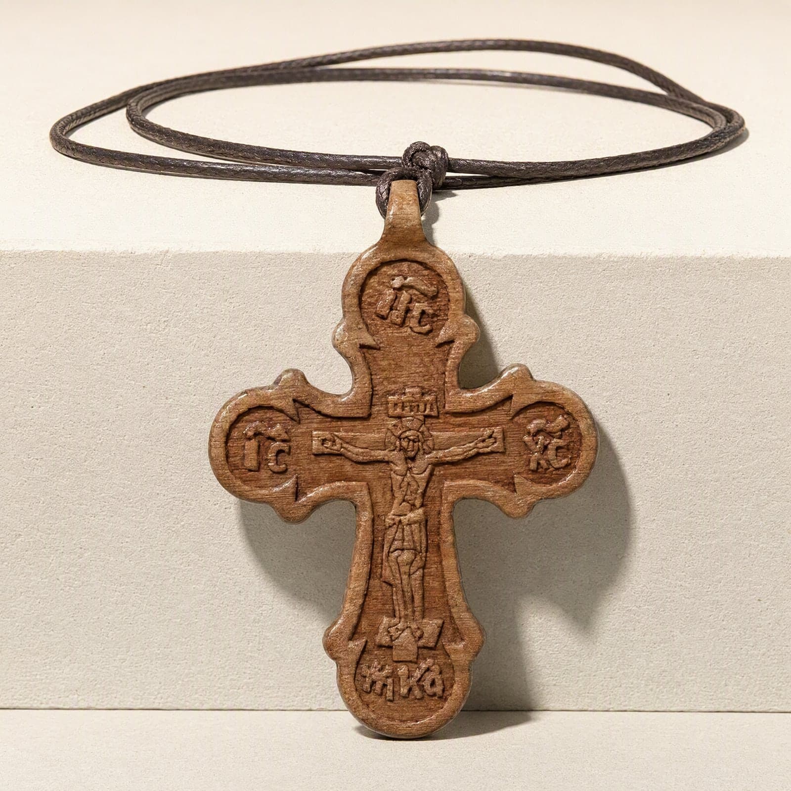 Orthodox Crucifix, wooden cross, hanging over the edge of a bone plaster plinth against a bone backdrop, on a thin dark cord.
