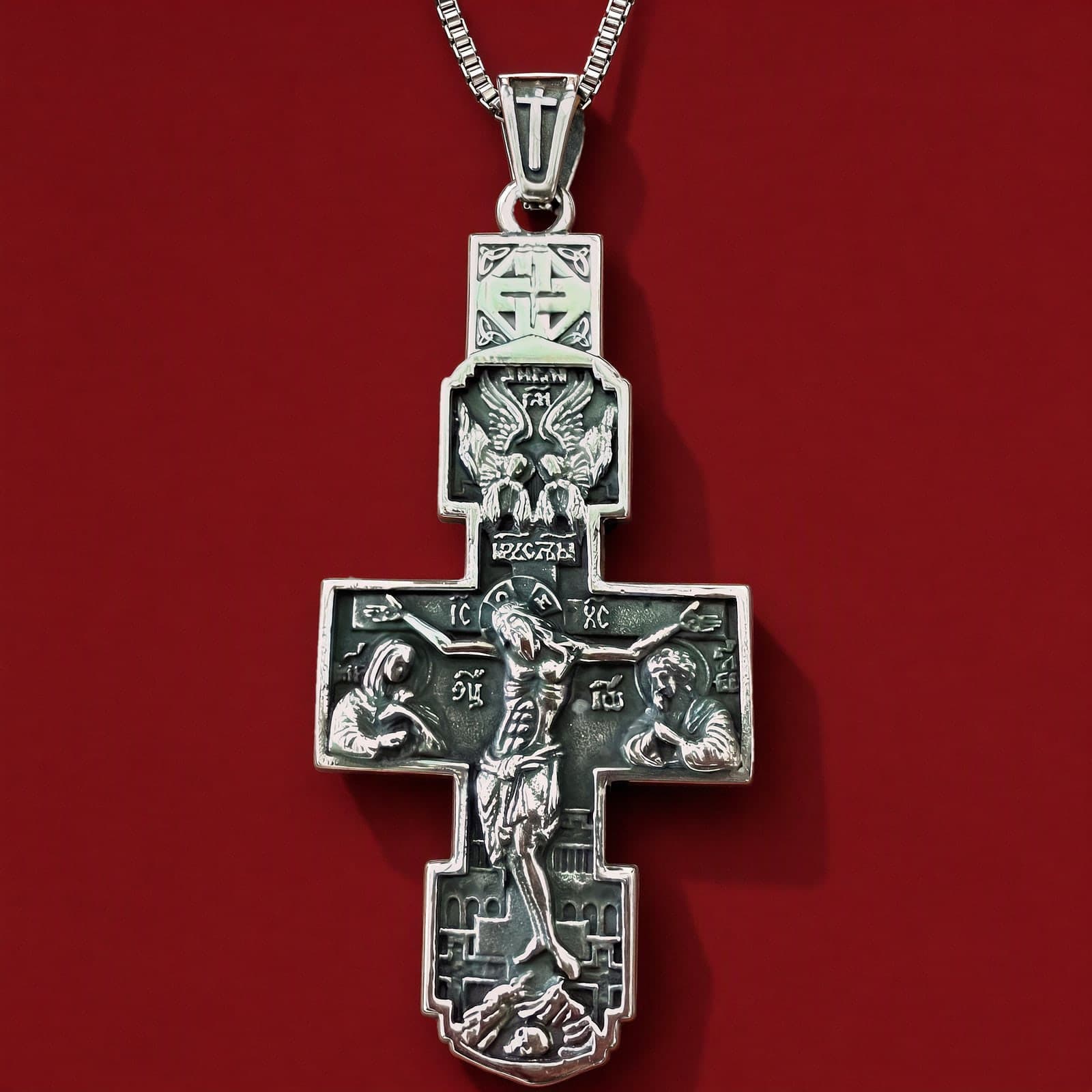 Orthodox Crucifix (Angels) - Silver Color - Stainless Steel Cross 70x39mm 20.2g: a silver-tone stainless steel stepped Orthodox crucifix with deep relief of the Crucifixion and a tall bail on a plain silver-tone box chain (shown on a chain), against an oxblood backdrop.
