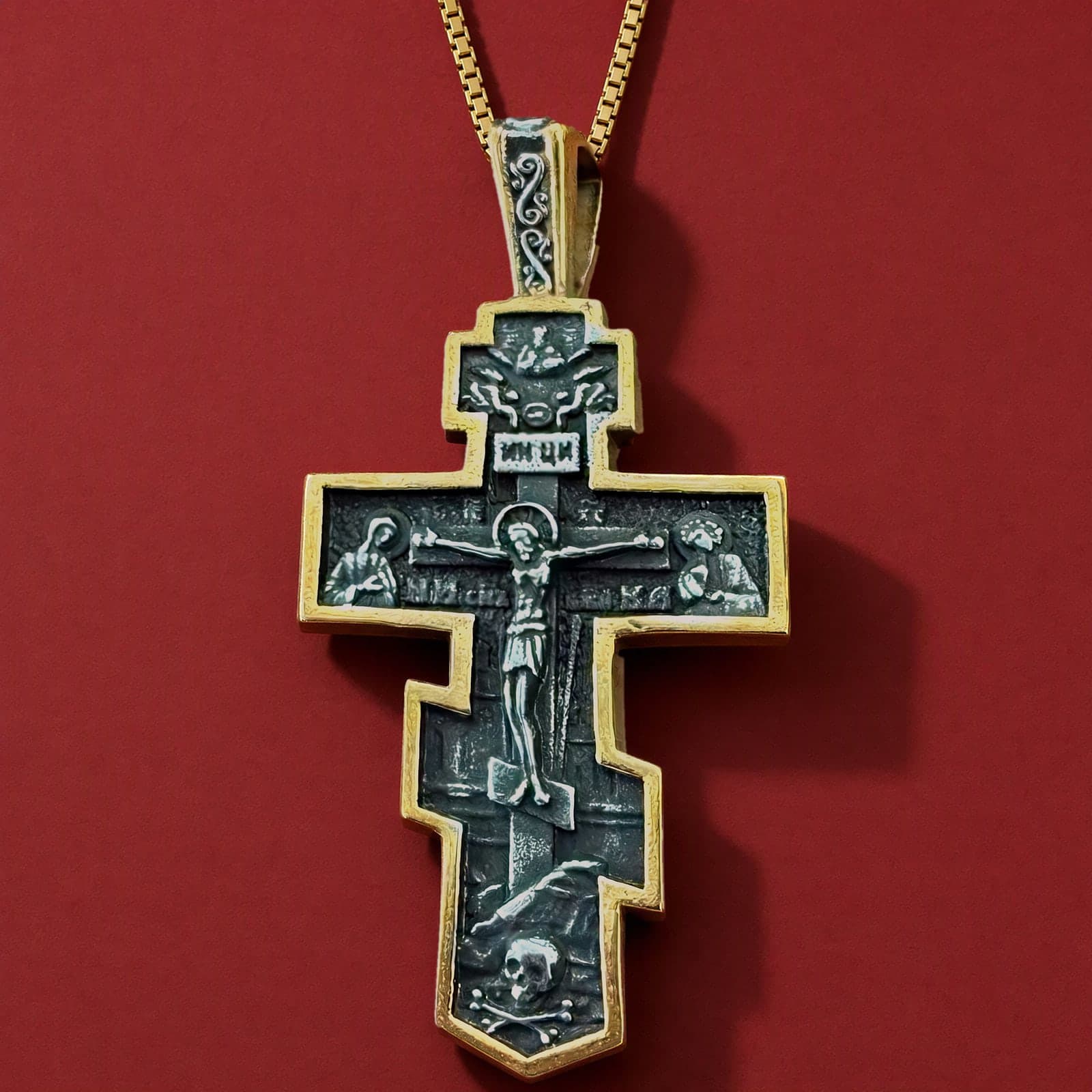 Orthodox Crucifix (Mary and St John) - Black&Gold Color - Stainless Steel Cross 70x39mm 20.2g: a black-and-gold stepped Orthodox crucifix with an ornamented gold-tone bail and blackened field with silver relief on a plain gold-tone box chain (shown on a chain), against an oxblood backdrop.