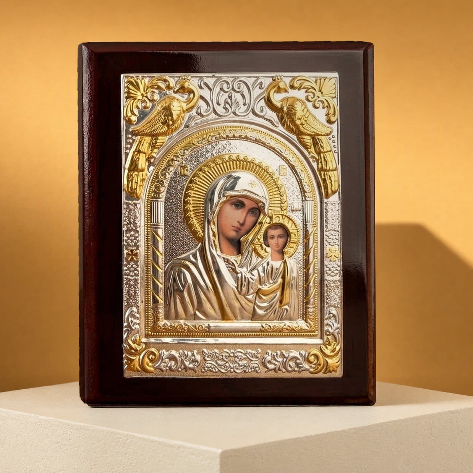 Orthodox Virgin Mary (Our Lady of Kazan, Rectangular) - Silver&Gold Color - Wooden Icon: a silver-and-gold foil icon of the Mother of God of Kazan in a dark wooden frame, on a white plinth against an ochre backdrop.