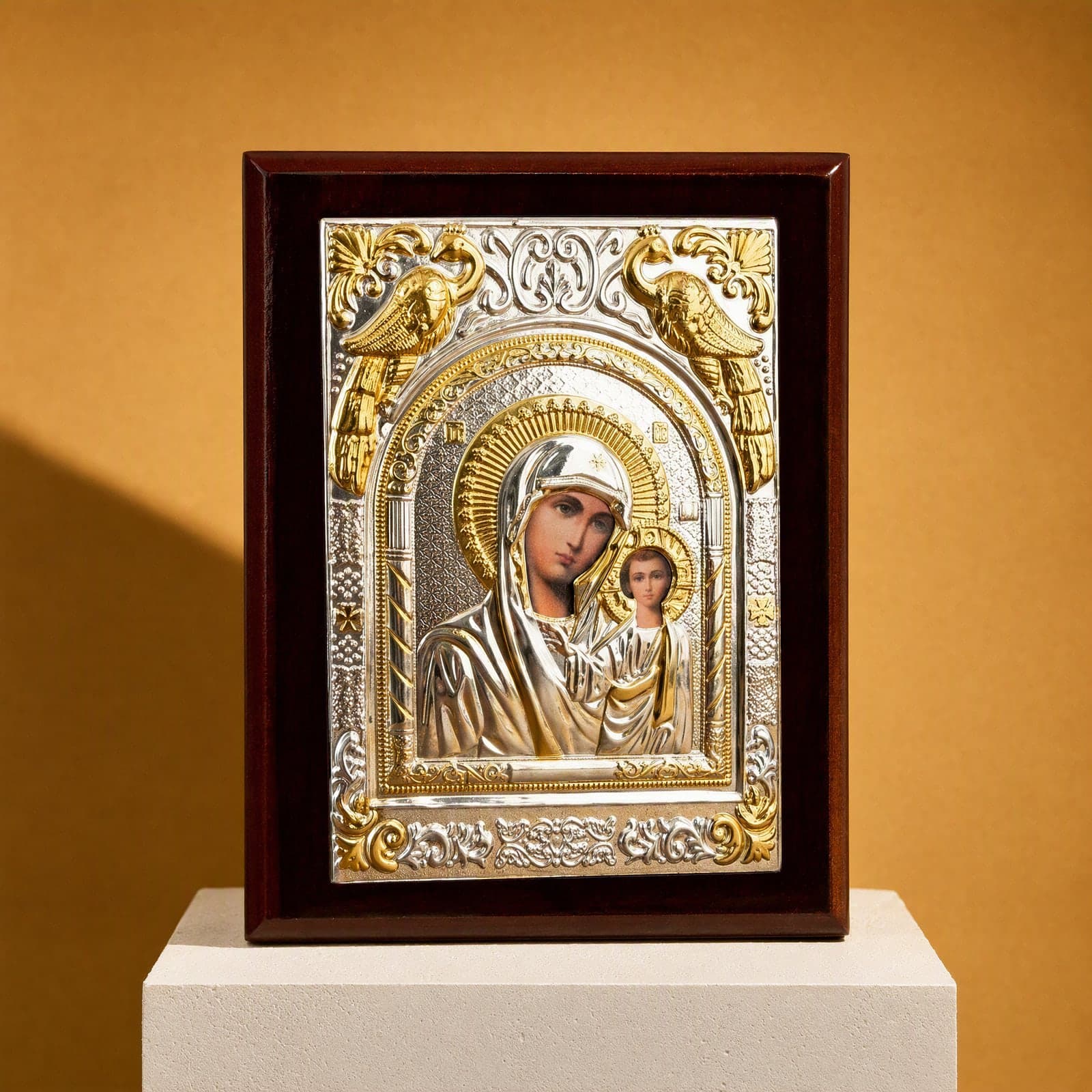 Orthodox Virgin Mary (Our Lady of Kazan, Rectangular), silver and gold wooden icon, standing on a bone plaster plinth against an ochre backdrop.