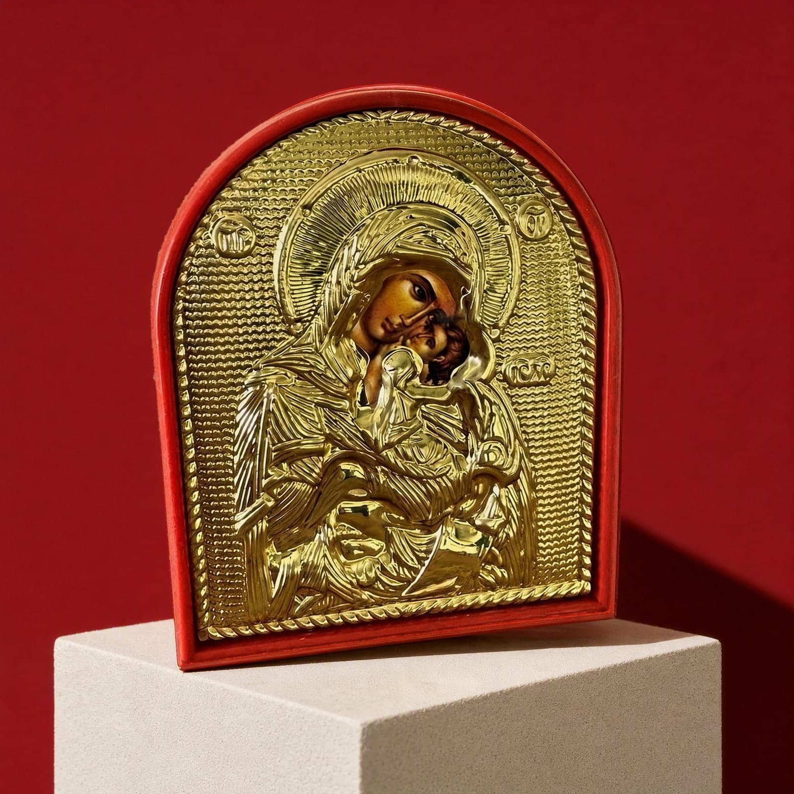 Orthodox Mother of God - Gold Color - Wooden Icon: an arched gold-foil icon of the Mother of God with a red rim, on a white plinth against an oxblood backdrop.