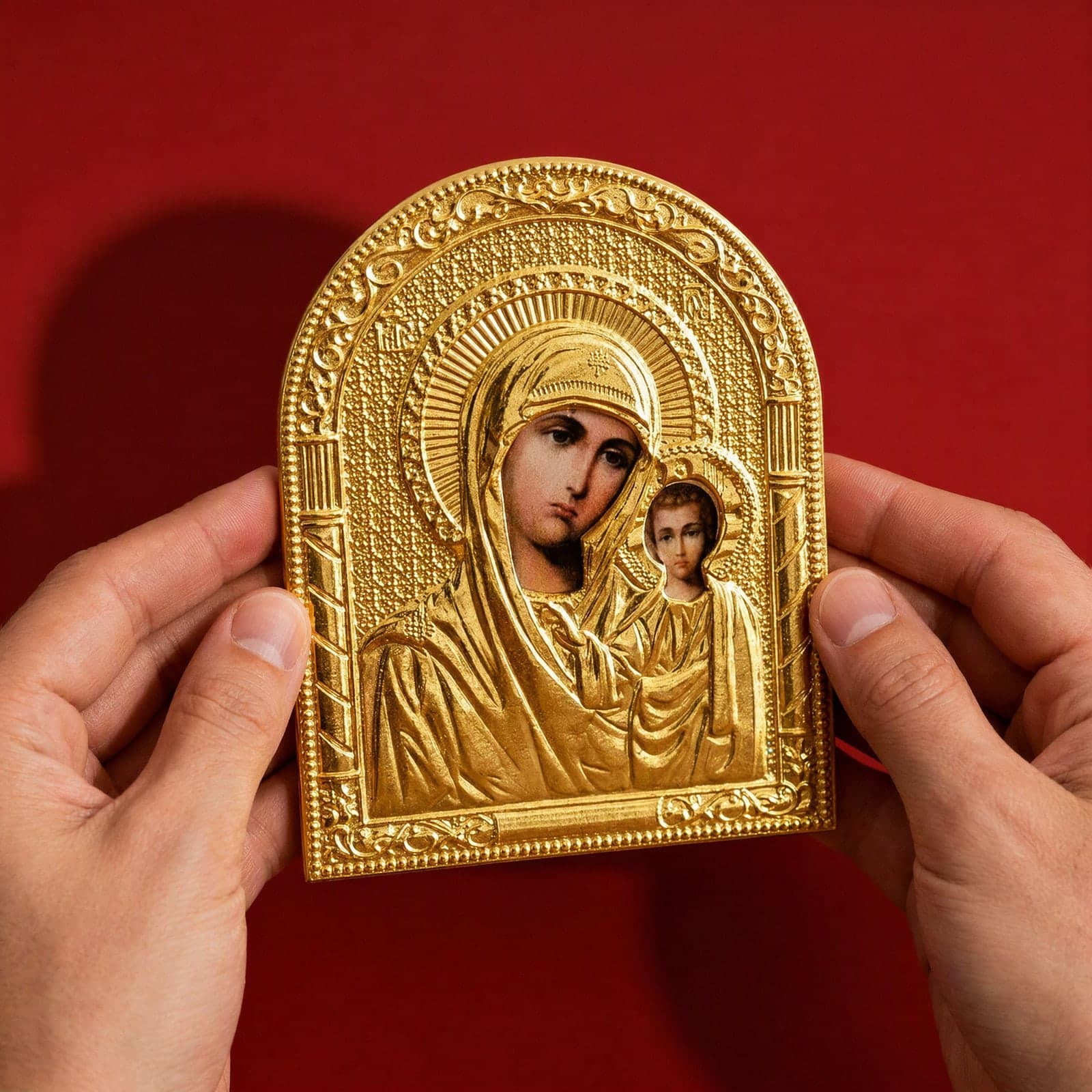 Orthodox Virgin Mary Holding Jesus, gold-tone icon held in both hands at its true size (14 x 10 cm).