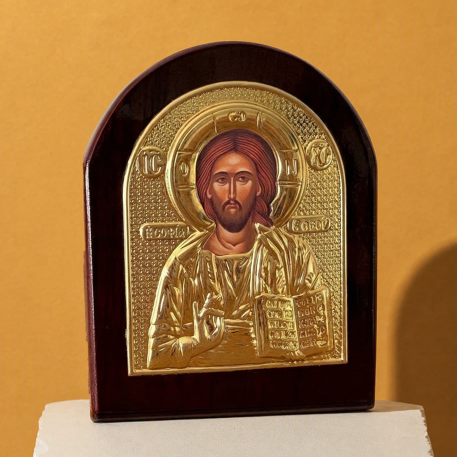 Orthodox Jesus Christ Pantocrator - Gold Color - Wooden Icon: an arched gold-foil icon of Christ Pantocrator on a dark wooden board, on a white plinth against an ochre backdrop.