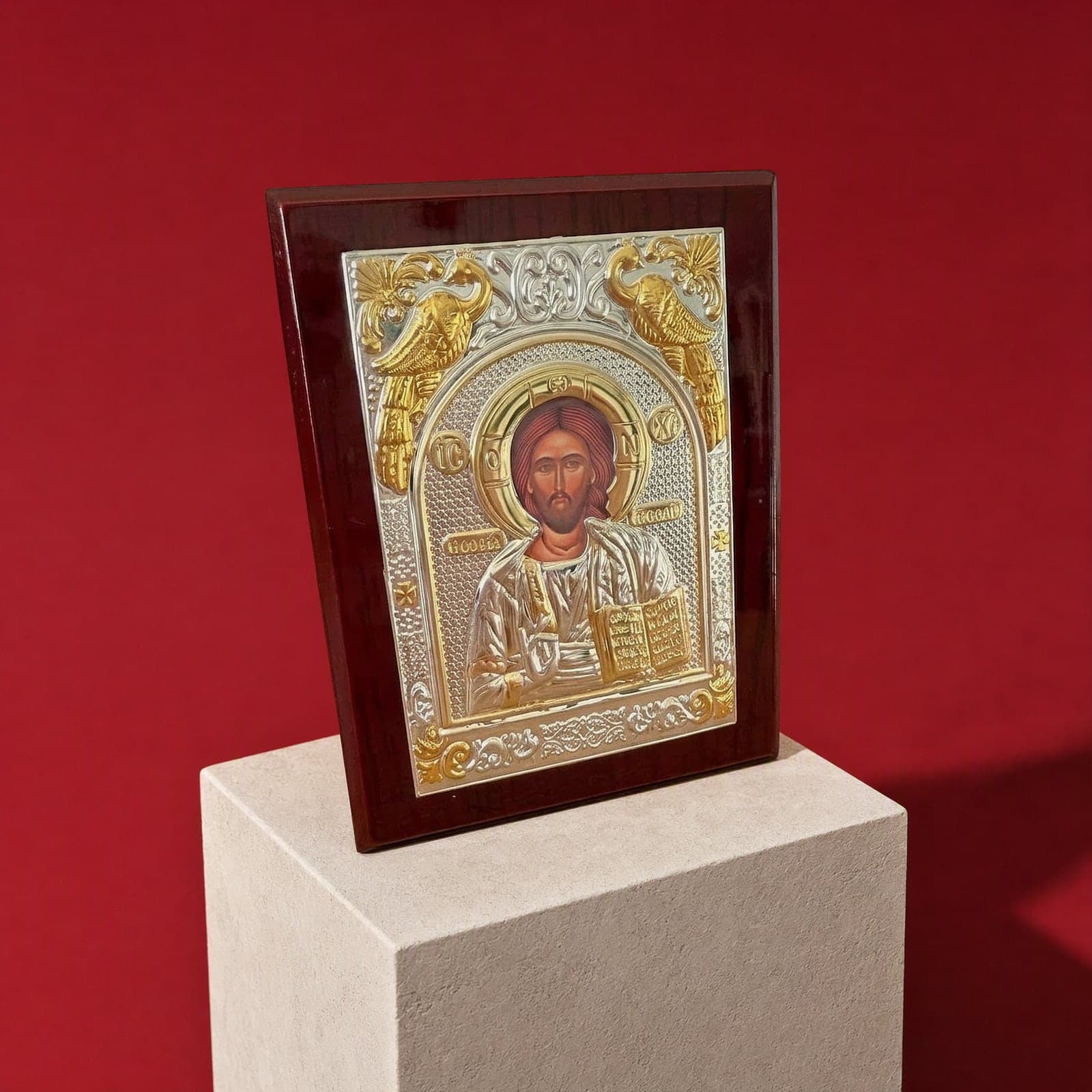 Orthodox Jesus Christ Pantocrator - Silver&Gold Color - Wooden Icon 12х9cm seen from a 45-degree angle on a white plinth.