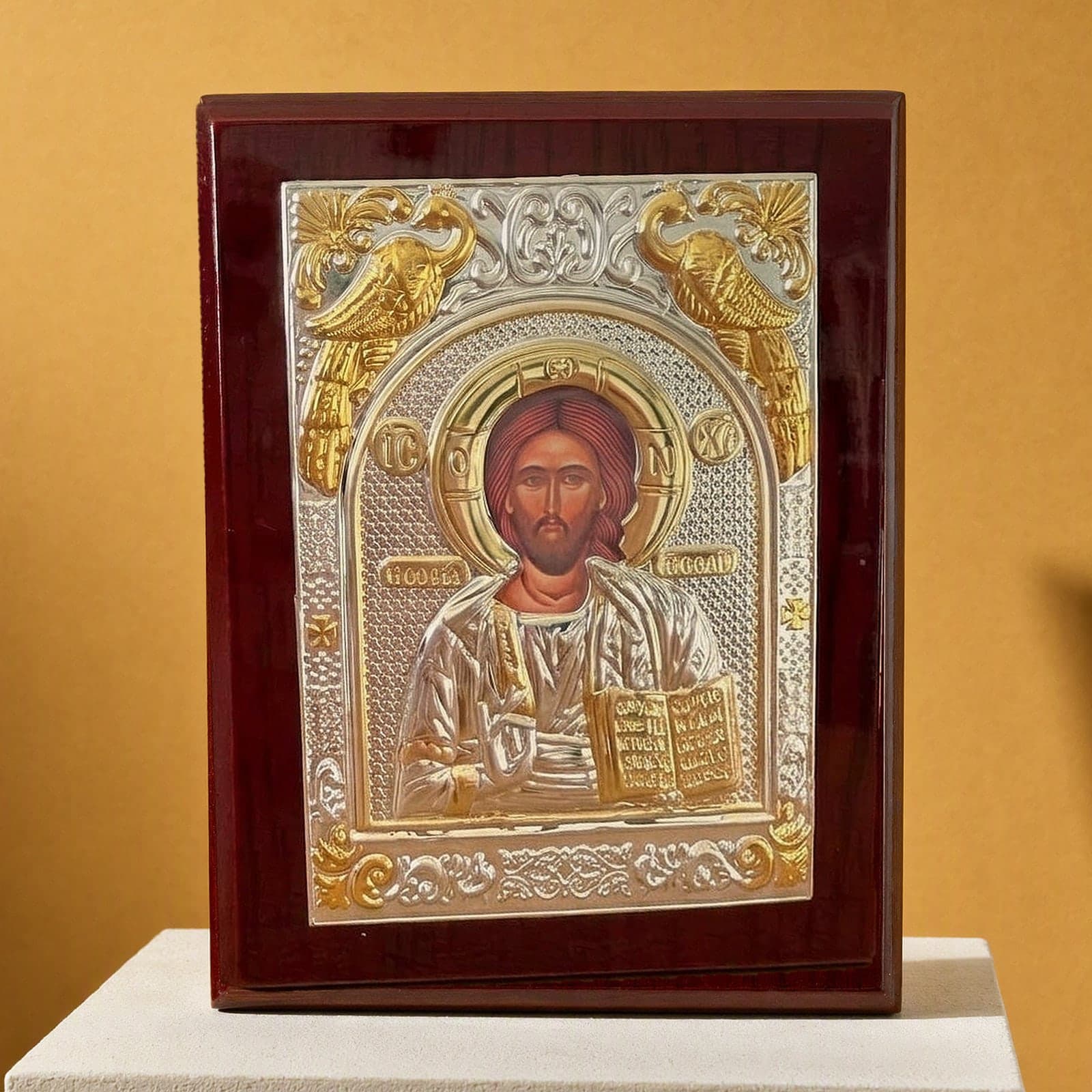 Orthodox Jesus Christ Pantocrator - Silver&Gold Color - Wooden Icon 12х9cm: a silver-and-gold foil icon of Christ Pantocrator in a dark wooden frame, on a white plinth against an ochre backdrop.