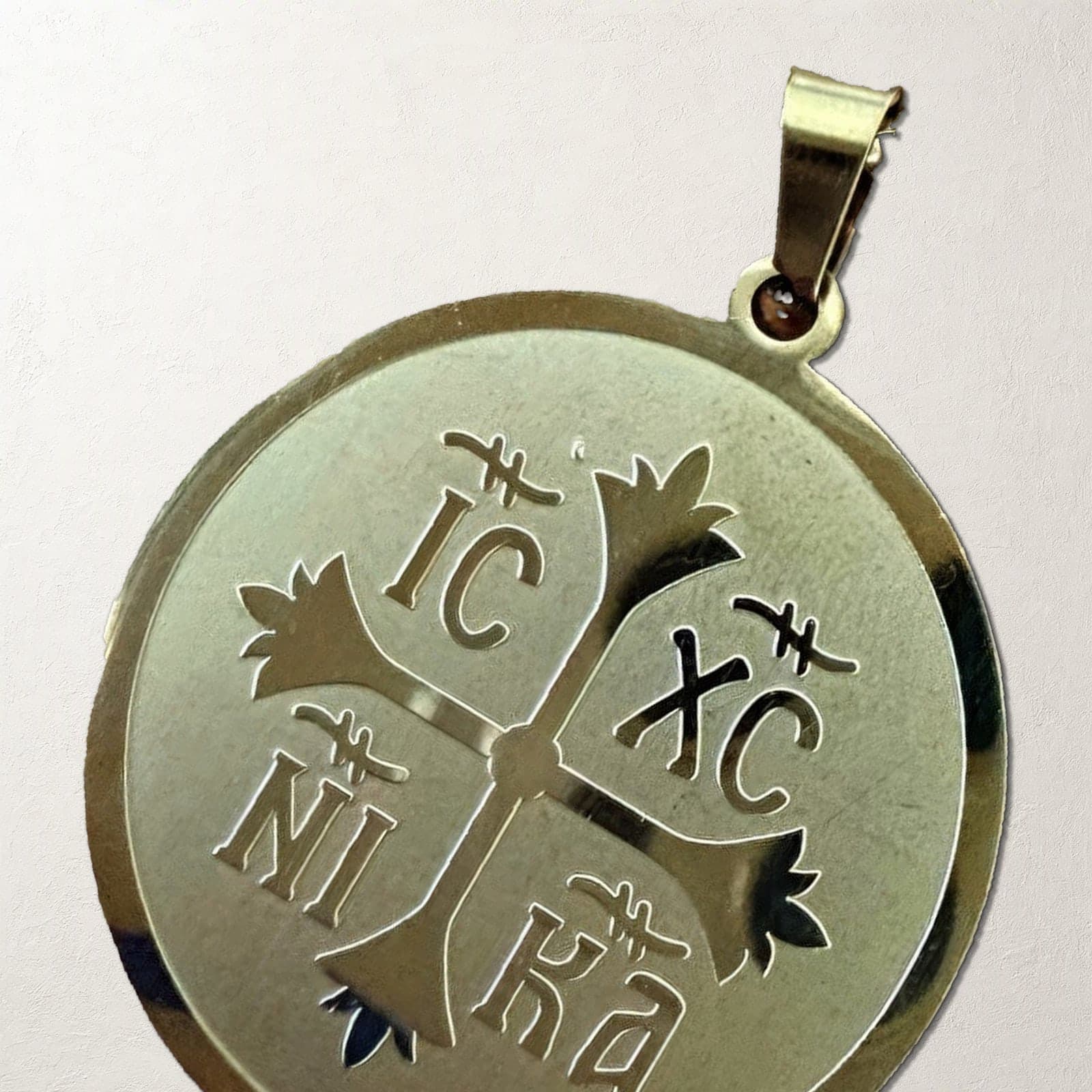 Close-up of the Orthodox IC XC NIKA - Gold Color - Stainless Steel Medallion on a white plaster surface.