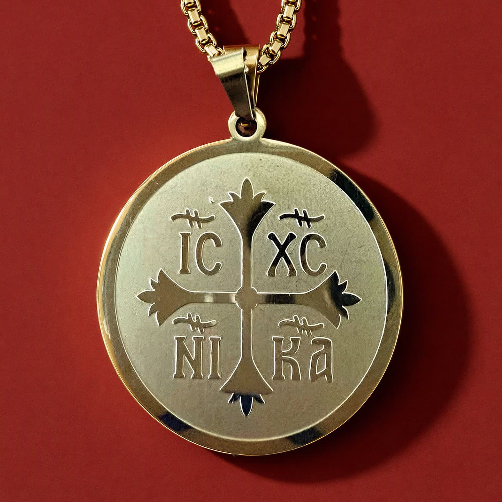 Orthodox IC XC NIKA - Gold Color - Stainless Steel Medallion: a round gold-tone stainless steel IC XC NIKA medallion on a gold-tone box chain, against an oxblood backdrop.