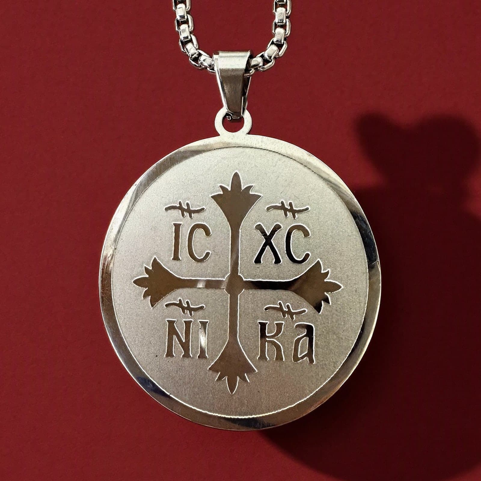 Orthodox IC XC NIKA - Silver Color - Stainless Steel Medallion: a round silver-tone stainless steel IC XC NIKA medallion on a silver-tone box chain, against an oxblood backdrop.