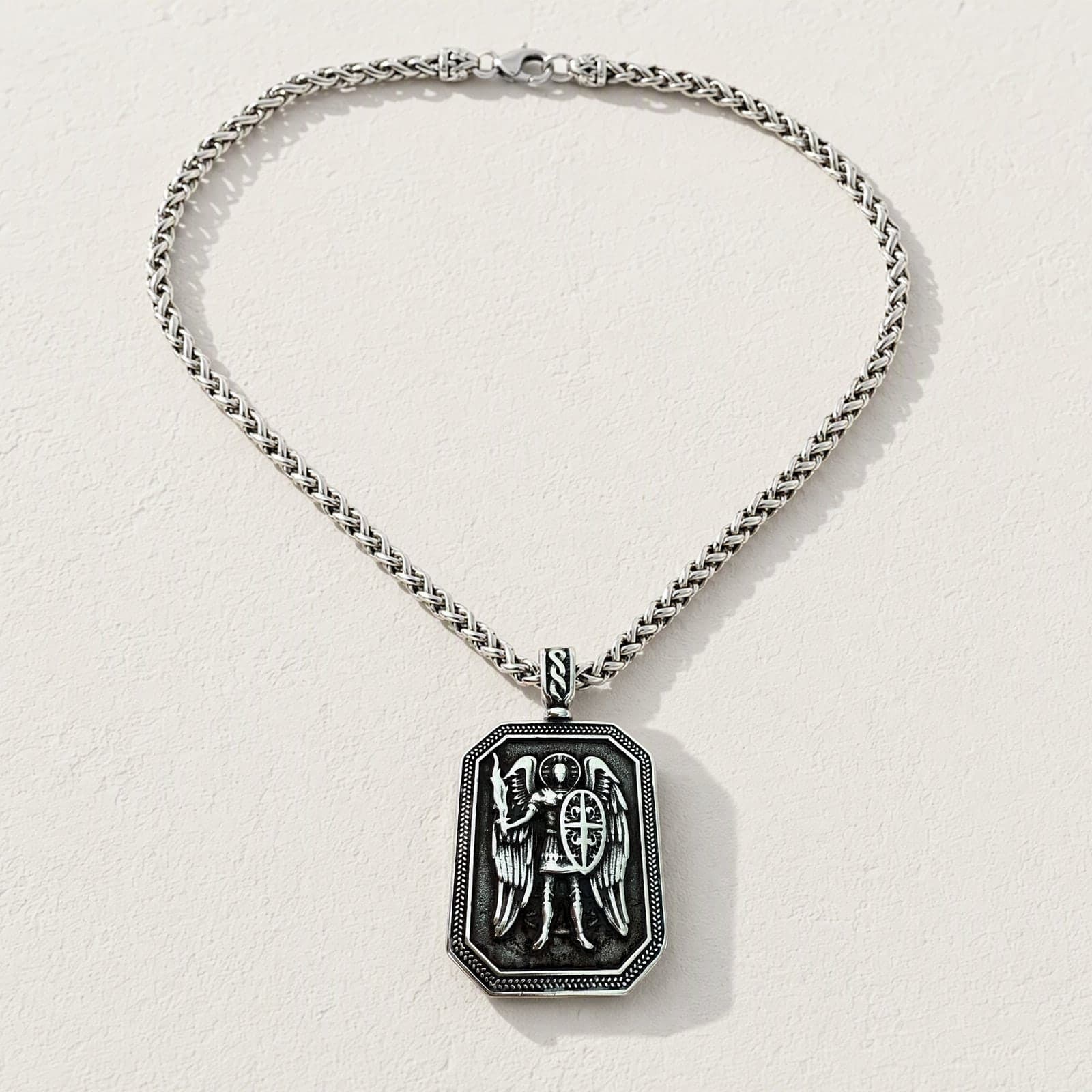 Orthodox St. Michael Archangel - Silver Color - Stainless Steel Medallion laid flat with its silver-tone wheat chain on a white plaster surface.
