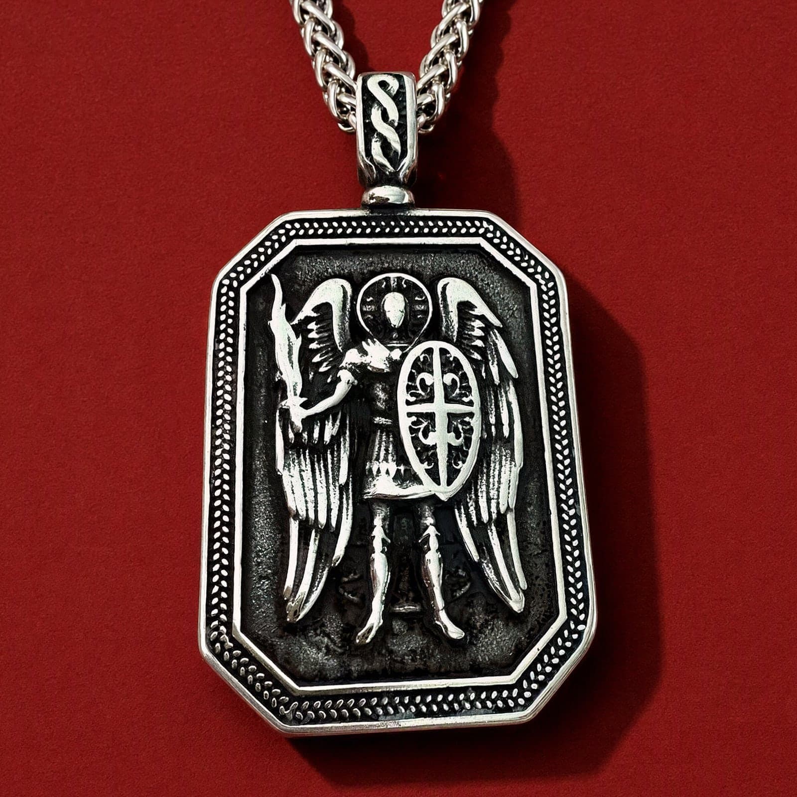 Orthodox St. Michael Archangel - Silver Color - Stainless Steel Medallion: an octagonal silver-tone stainless steel St Michael the Archangel medallion with relief of the Archangel with sword and shield on a silver-tone wheat chain, against an oxblood backdrop.