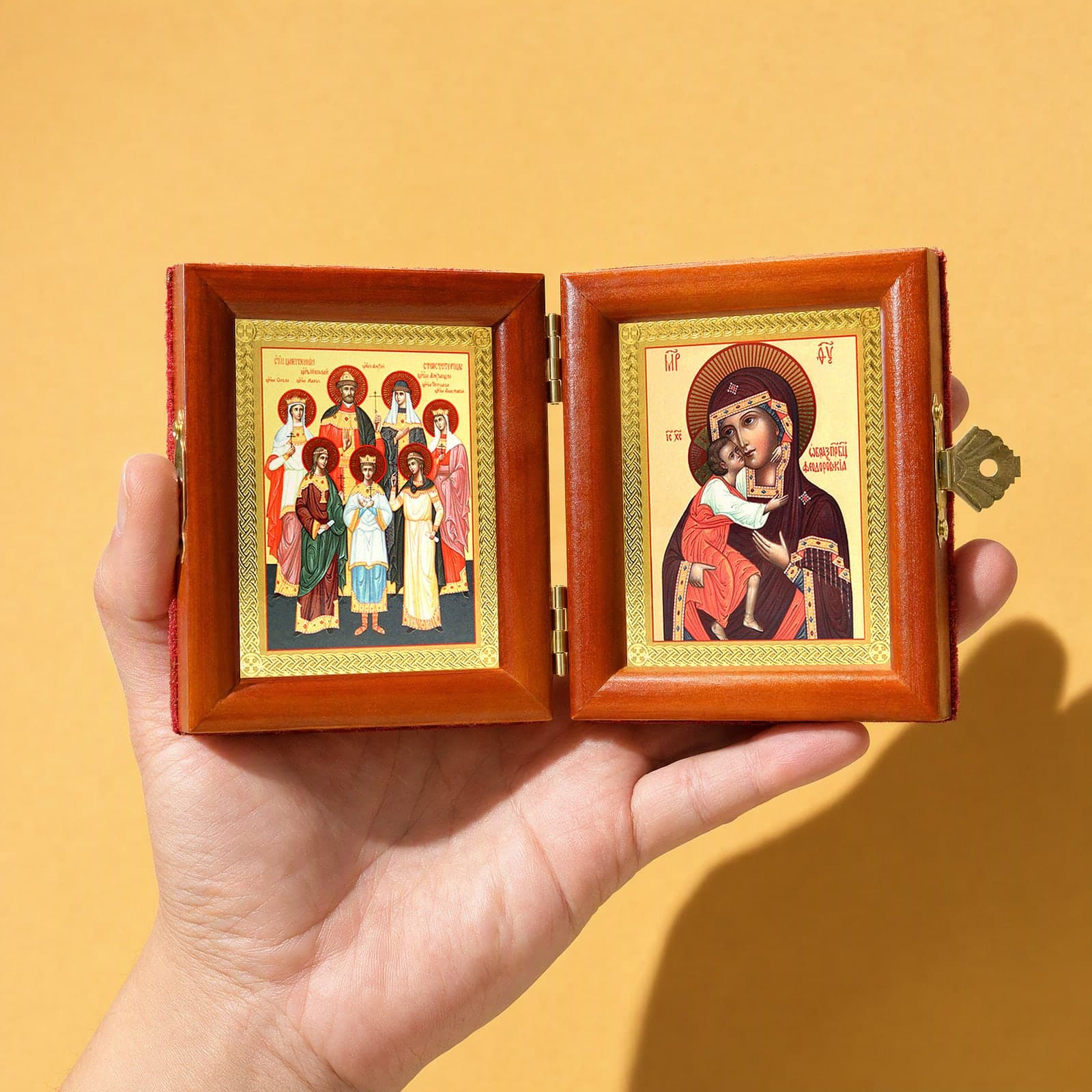 Royal Passion-Bearers (Romanov family) & Feodorovskaya Mother of God travel diptych held open in one hand to show its size: 16.5 cm wide open, about two palm widths.