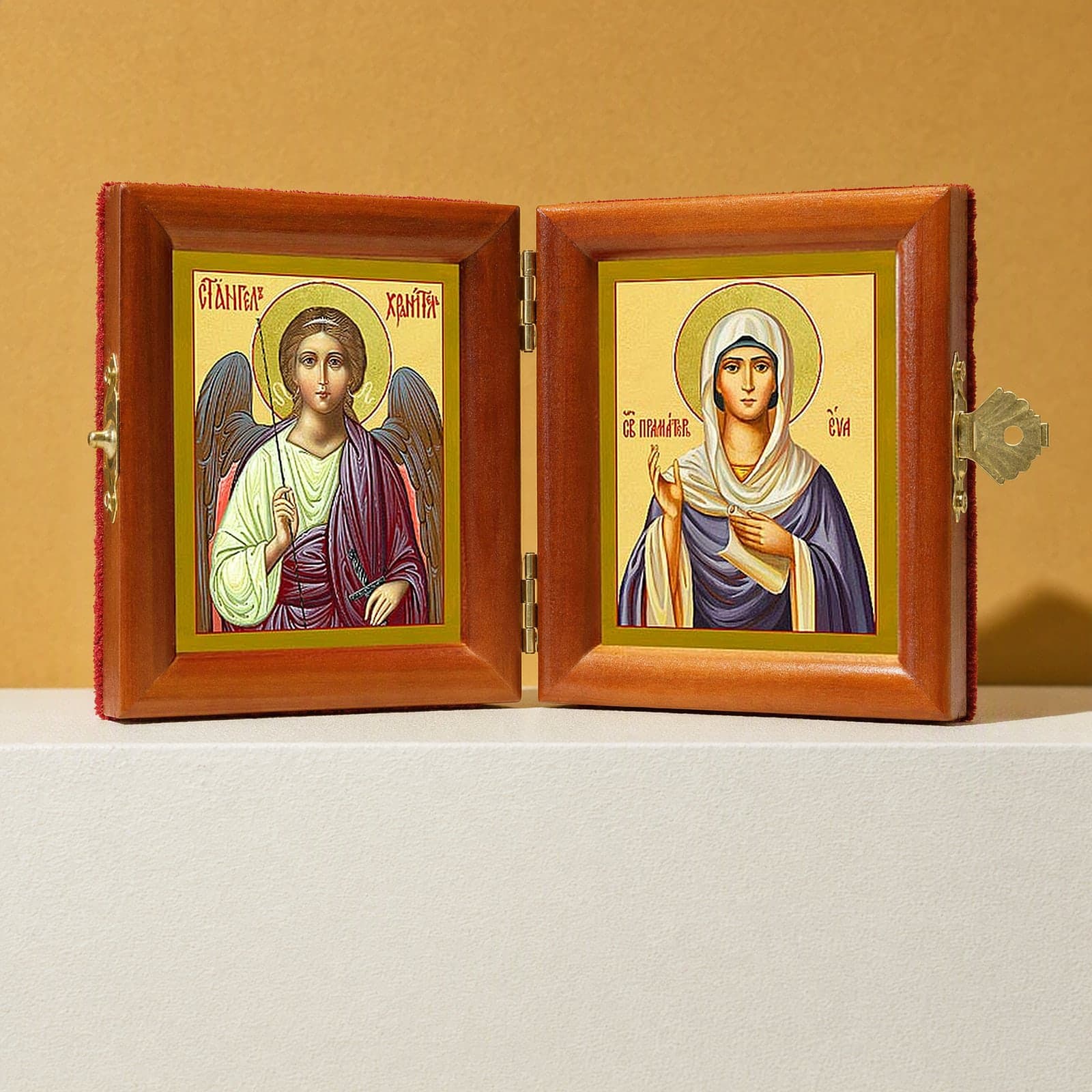 Holy Foremother Eve & Guardian Angel name diptych, open: folding diptych of the Guardian Angel and the Holy Foremother Eve in honey pine frames with brass hinges and clasp, on a white plinth against an ochre backdrop.