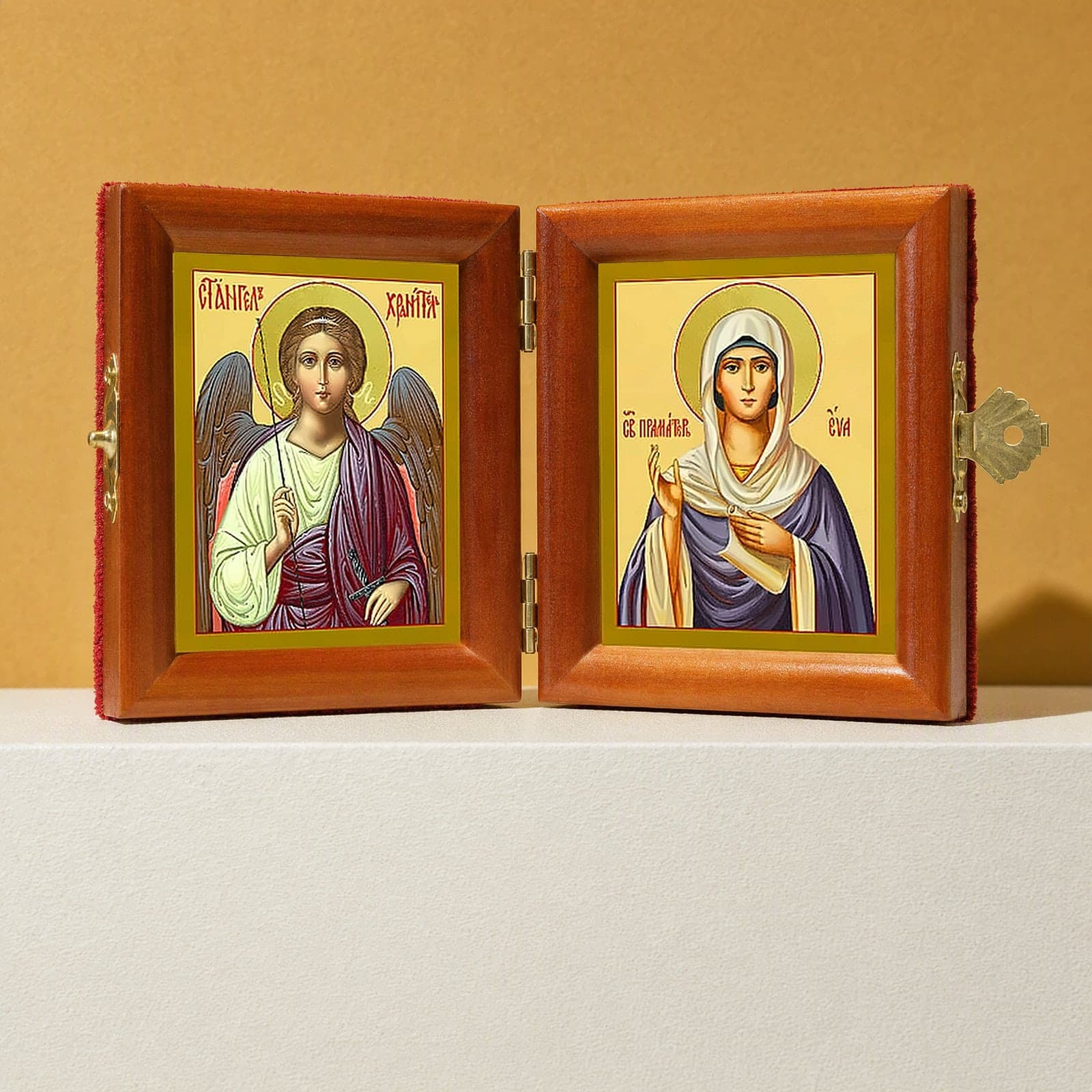 Holy Foremother Eve & Guardian Angel name diptych, open: folding diptych of the Guardian Angel and the Holy Foremother Eve in honey pine frames with brass hinges and clasp, on a white plinth against an ochre backdrop.