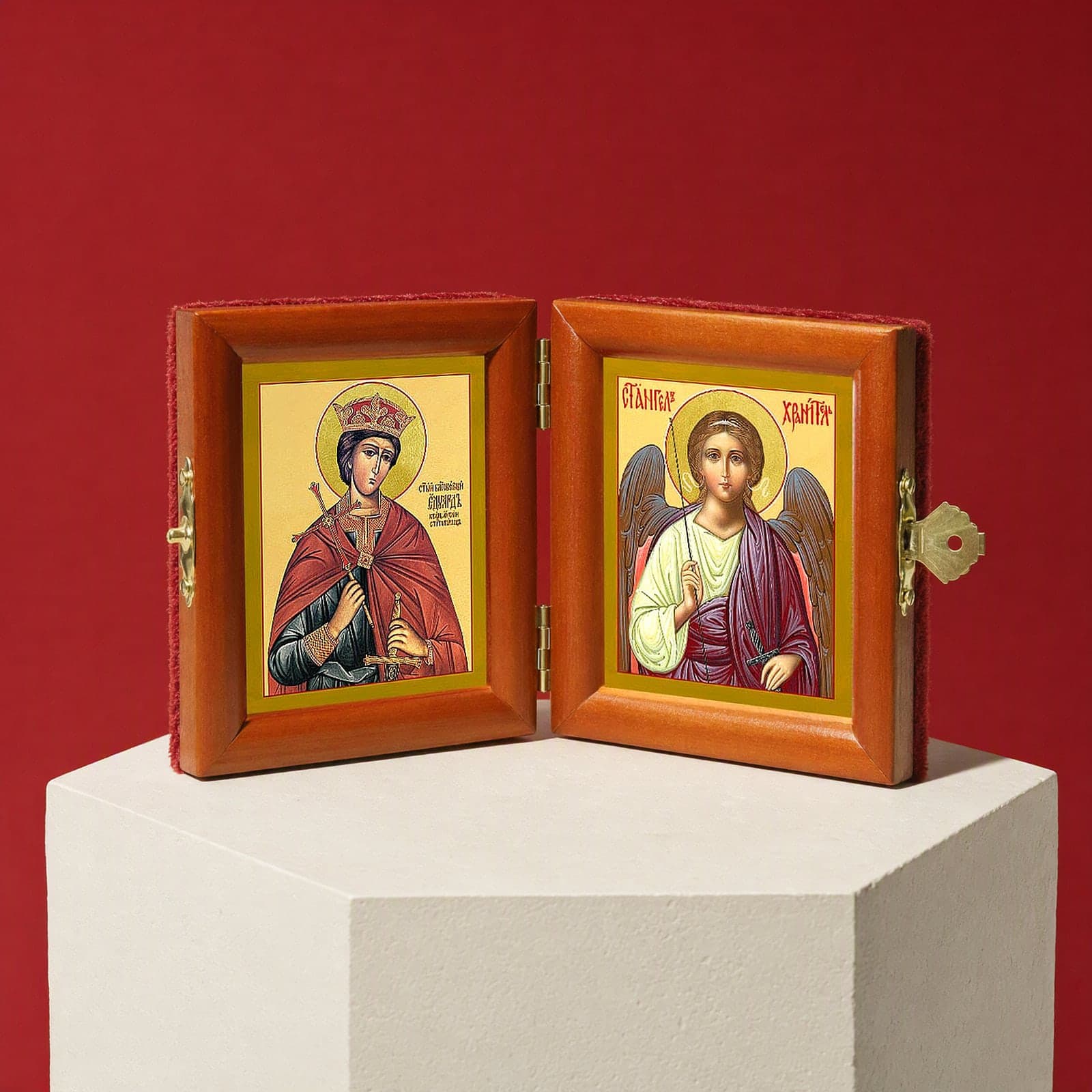 St Edward the Martyr, King of England & Guardian Angel name diptych seen from a 45-degree angle, half open on a white plinth against an oxblood backdrop, showing the frame depth and hinges.