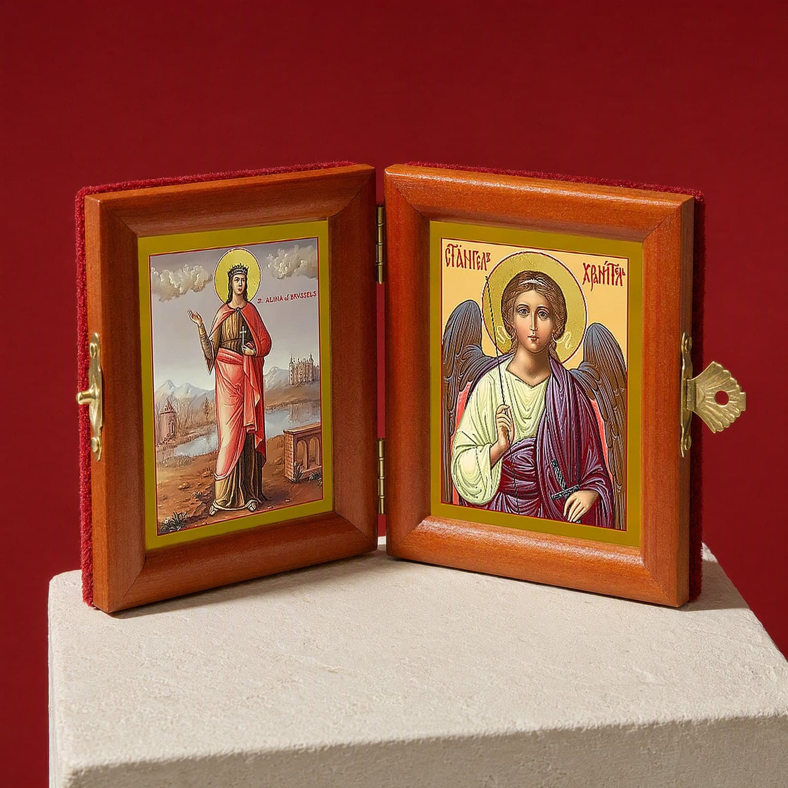 St Alina (Alena) of Brussels & Guardian Angel name diptych seen from a 45-degree angle, half open on a white plinth against an oxblood backdrop, showing the frame depth and hinges.