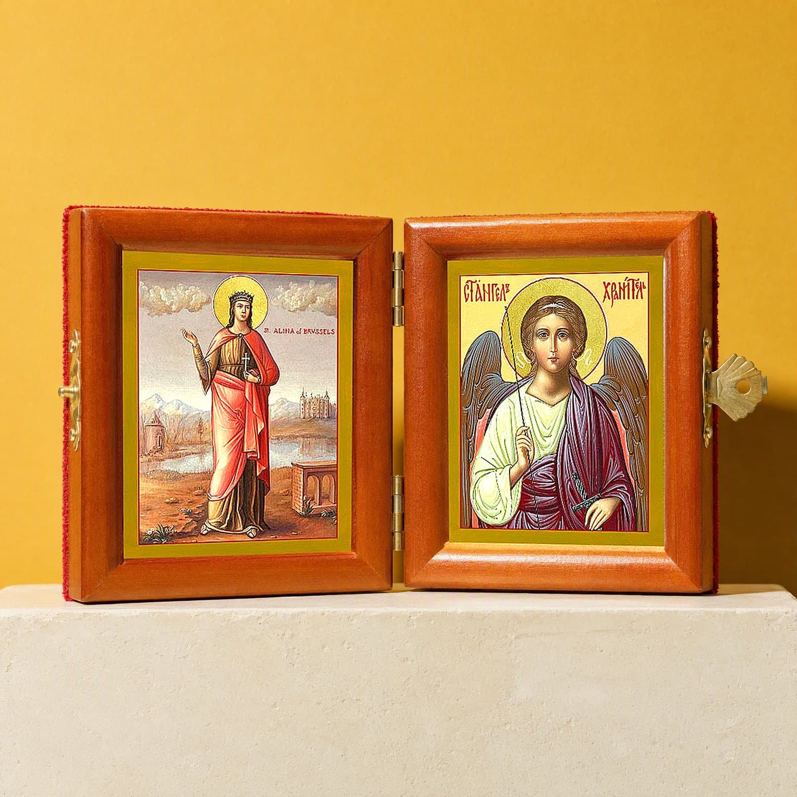 St Alina (Alena) of Brussels & Guardian Angel name diptych, open: folding diptych of St Alina of Brussels and the Guardian Angel in honey pine frames with brass hinges and clasp, on a white plinth against an ochre backdrop.