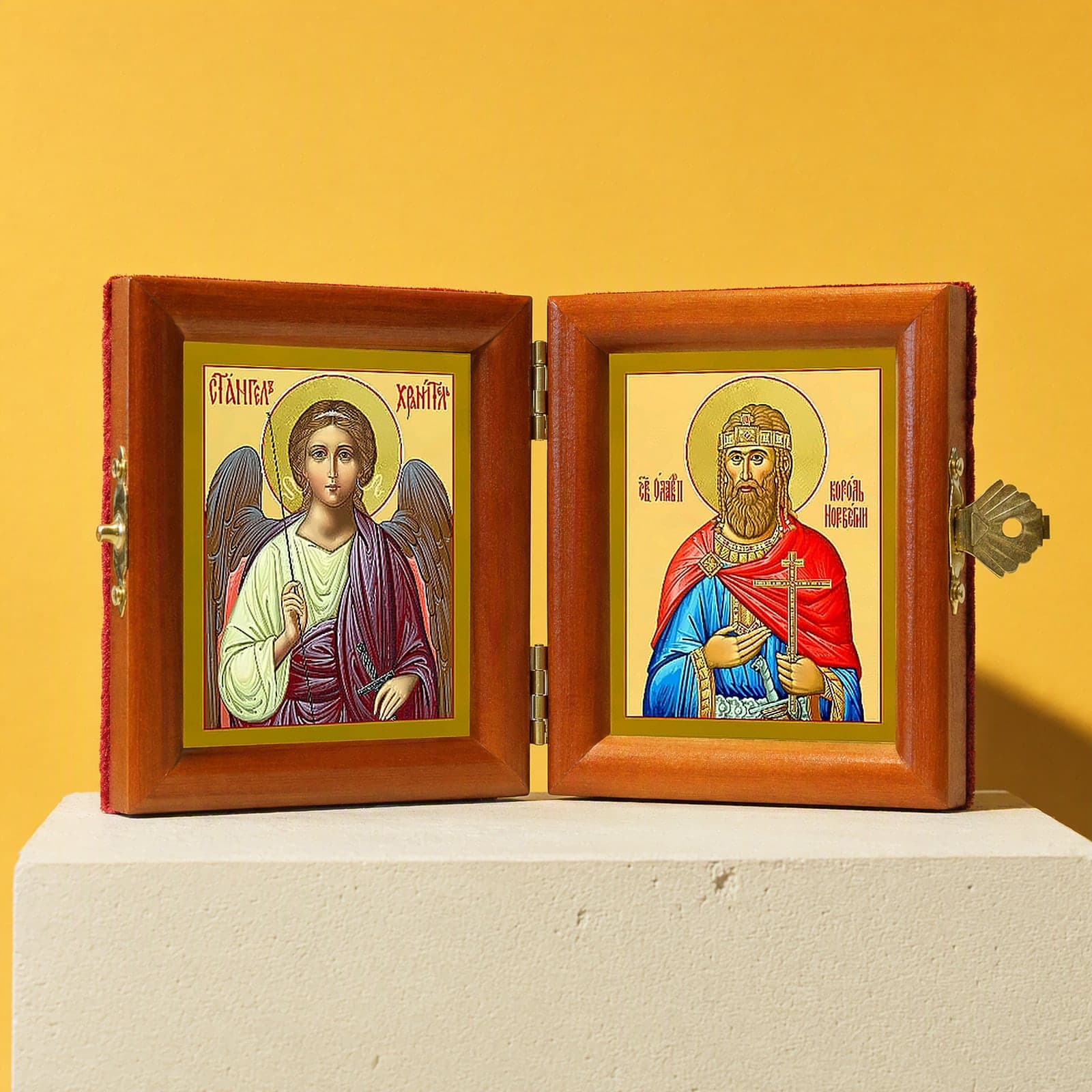 Именной складень «Святой Олаф, король Норвежский, и Ангел Хранитель», раскрытый: складень с Ангелом Хранителем и святым Олафом, королём Норвежским, в короне; рамки из медовой сосны, латунные петли и застёжка; на белой подставке на охристом фоне.