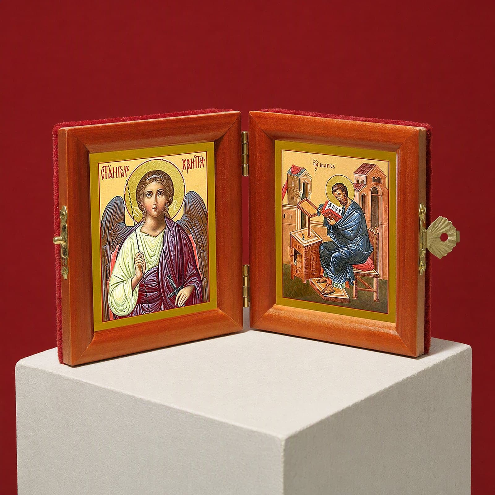 St Mark the Apostle & Guardian Angel name diptych seen from a 45-degree angle, half open on a white plinth against an oxblood backdrop, showing the frame depth and hinges.