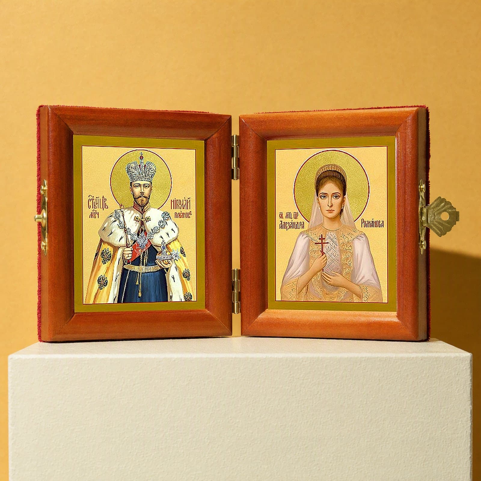 Sts Nicholas II & Alexandra (Royal Passion-Bearers) diptych, open: folding diptych of St Nicholas II the passion-bearer and St Alexandra the passion-bearer, Empress in honey pine frames with brass hinges and clasp, on a white plinth against an ochre backdrop.