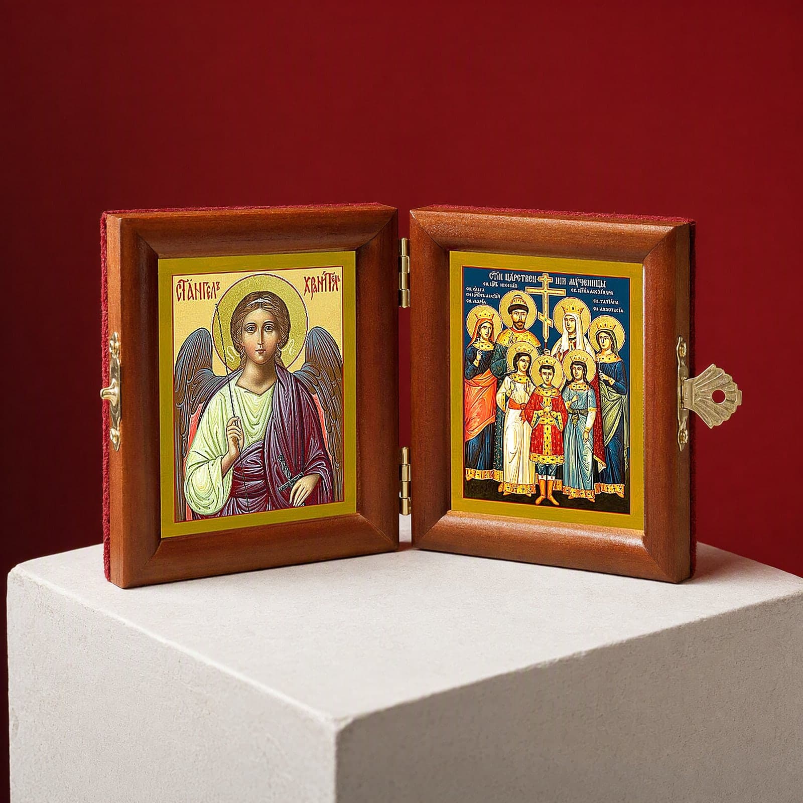 Royal Passion-Bearers (Romanov family) & Guardian Angel name diptych seen from a 45-degree angle, half open on a white plinth against an oxblood backdrop, showing the frame depth and hinges.